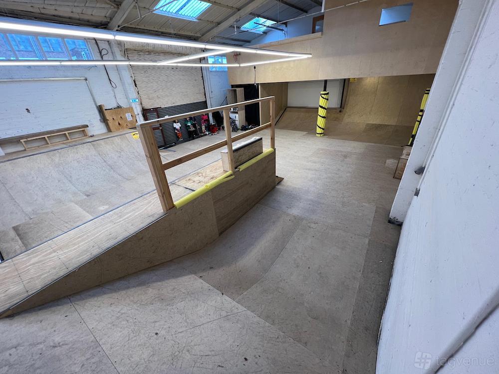 An indoor event space with wooden ramps, high ceilings, and fluorescent lighting at School of Skate Copeland Park.