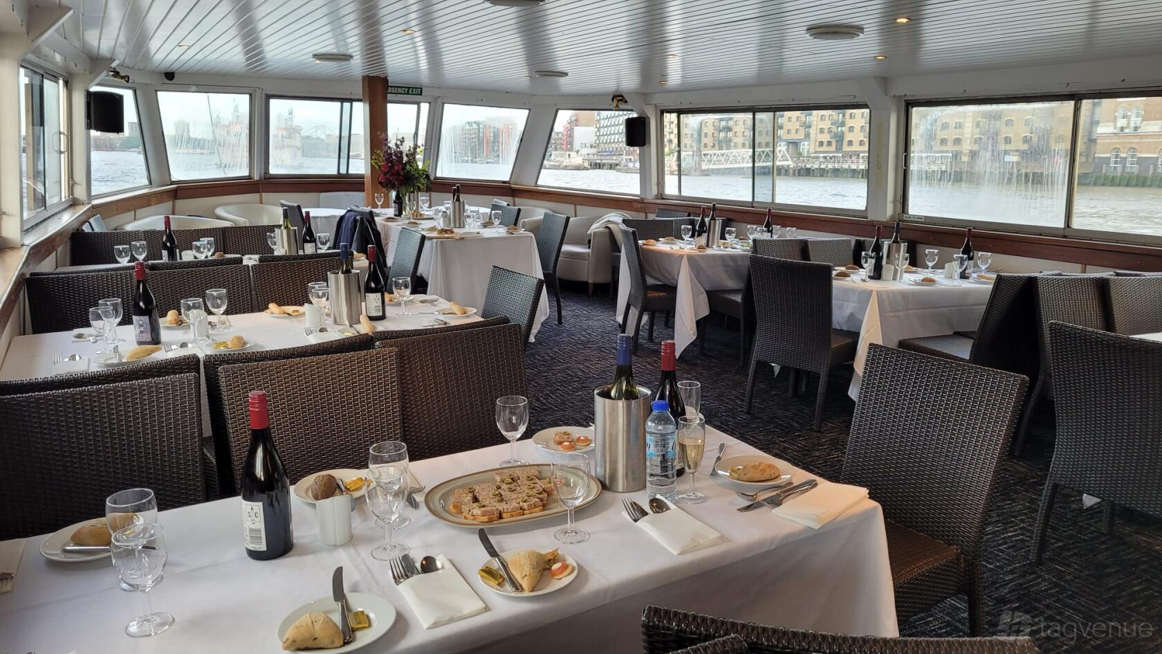 A boat dining area with large windows, white tablecloths, and set tables overlooking the river at City Cruises Ltd MV Westminster.