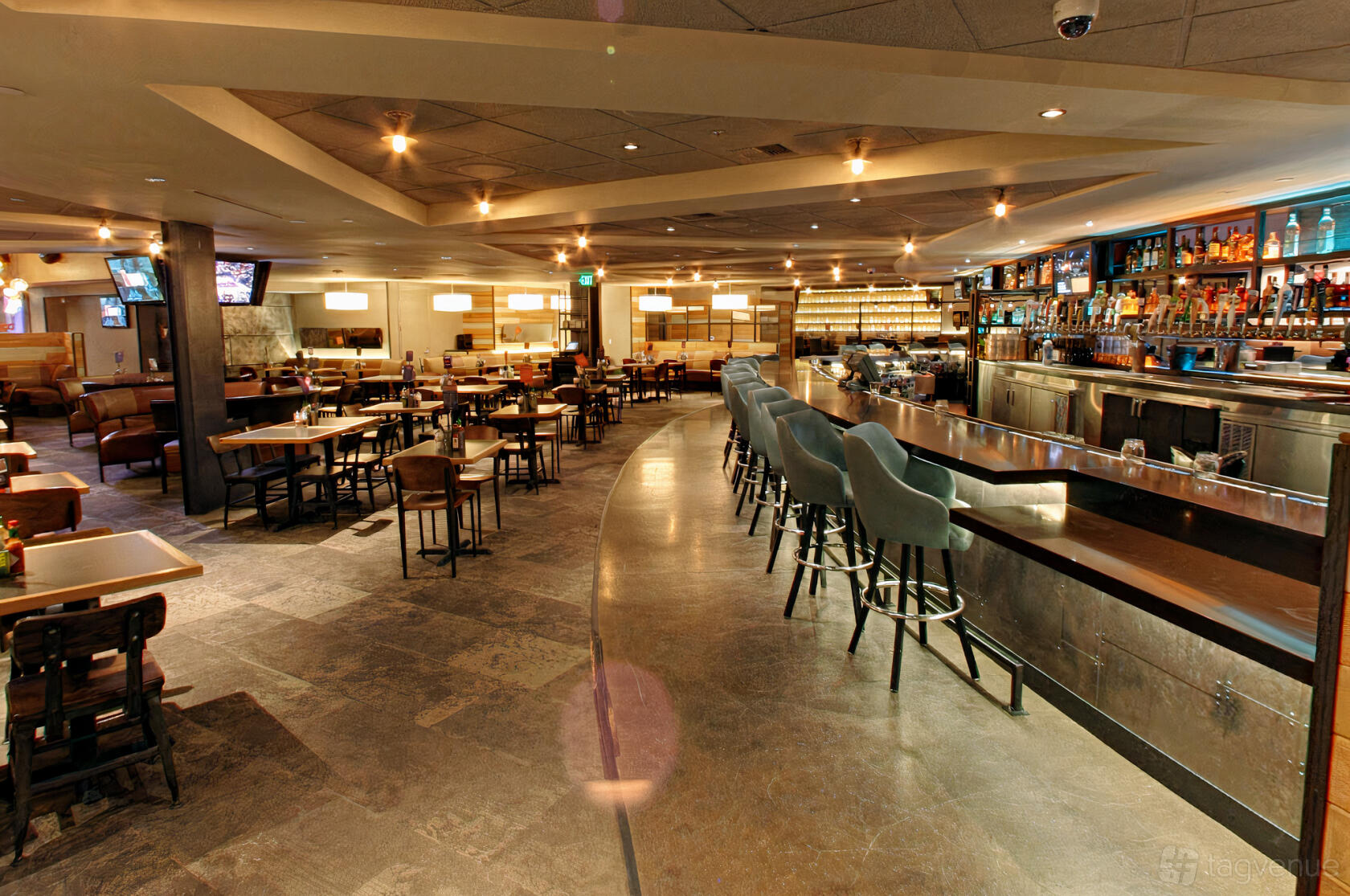 A dining room in a bar with a long curved bar counter, high-backed stools, and rows of tables at Tom's Watch Bar Los Angeles.