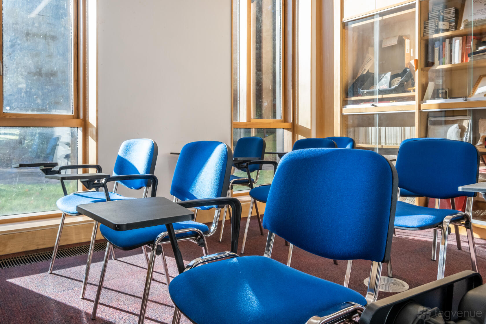 A classroom with blue chairs, individual writing tablets, and large windows letting in natural light at Ruskin Venues.