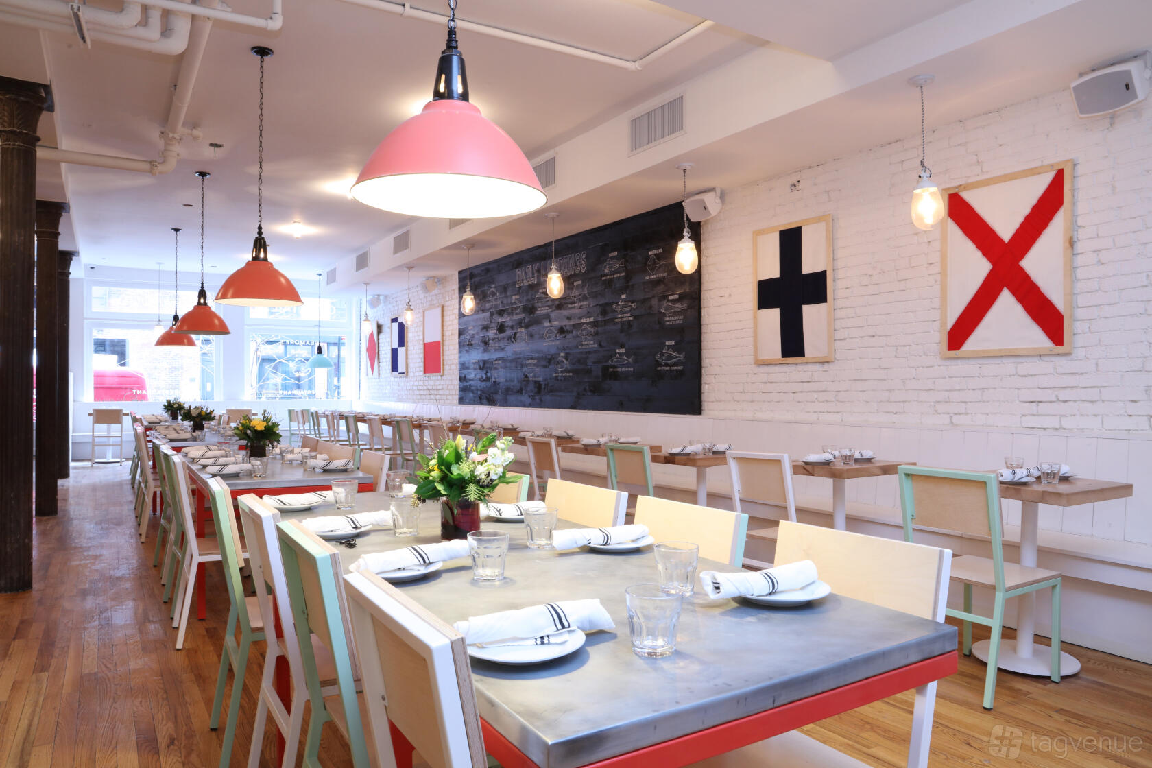 A dining room with nautical flag wall art, wooden floors, and long tables with pastel chairs at Seamore's Dumbo.