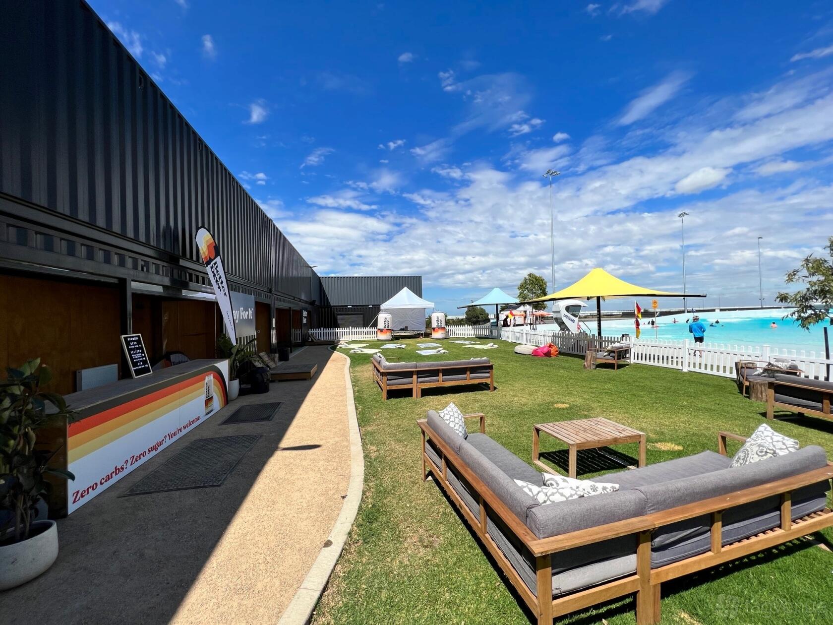An outdoor event venue with lounge seating, grass lawn, and umbrellas near a pool at URBNSURF.