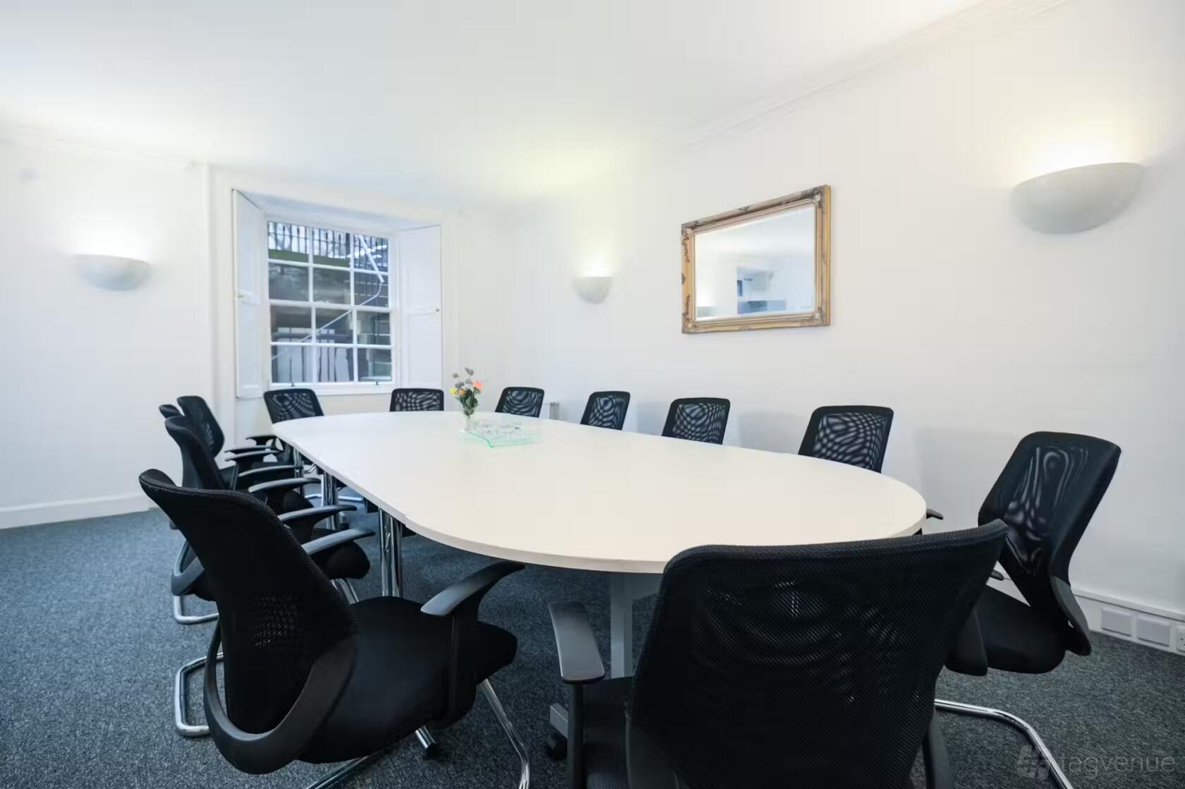 A boardroom with a large oval table, black mesh chairs, and natural light from sash windows at Citibase Edinburgh St Colme.
