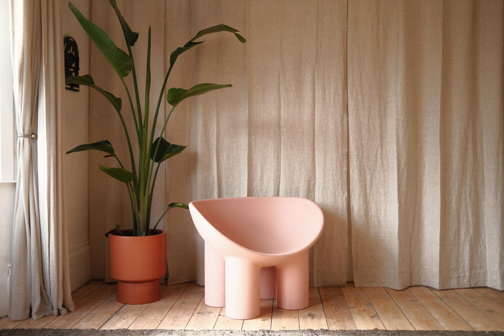 A photo studio with natural light, a blush pink sculptural chair, wooden flooring, and a potted plant at Groovy House.