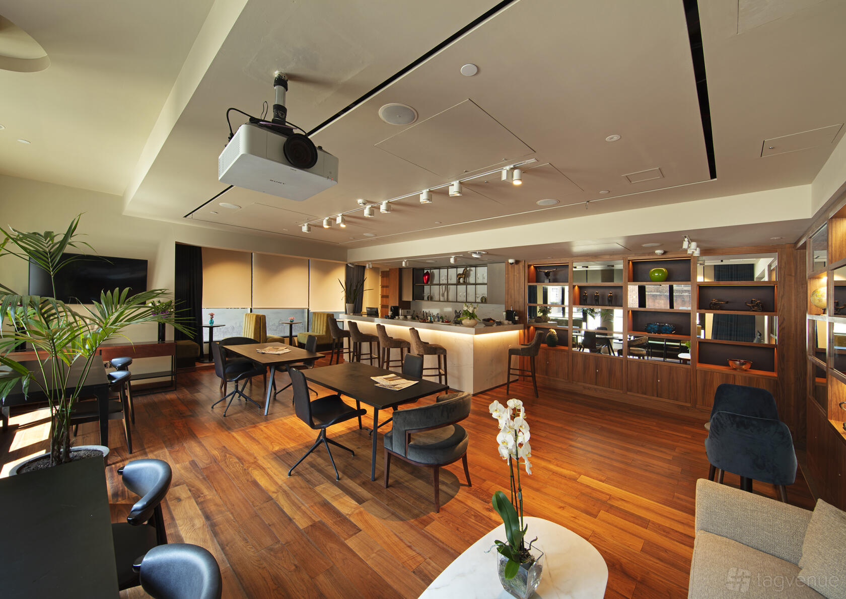 A hotel meeting room with wooden floors, built-in shelving, modern lighting, and a projection system at Tower Suites by Blue Orchid.