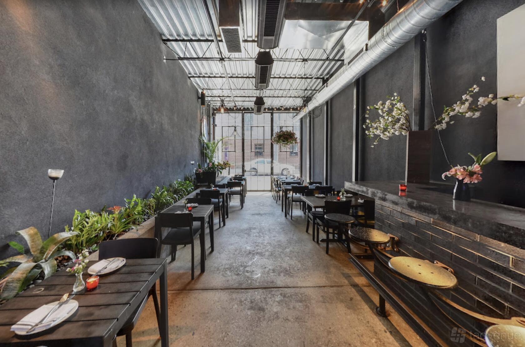 An event space in a bar with concrete floors, black chairs, potted plants, and industrial ceiling at Jerry's Bar.