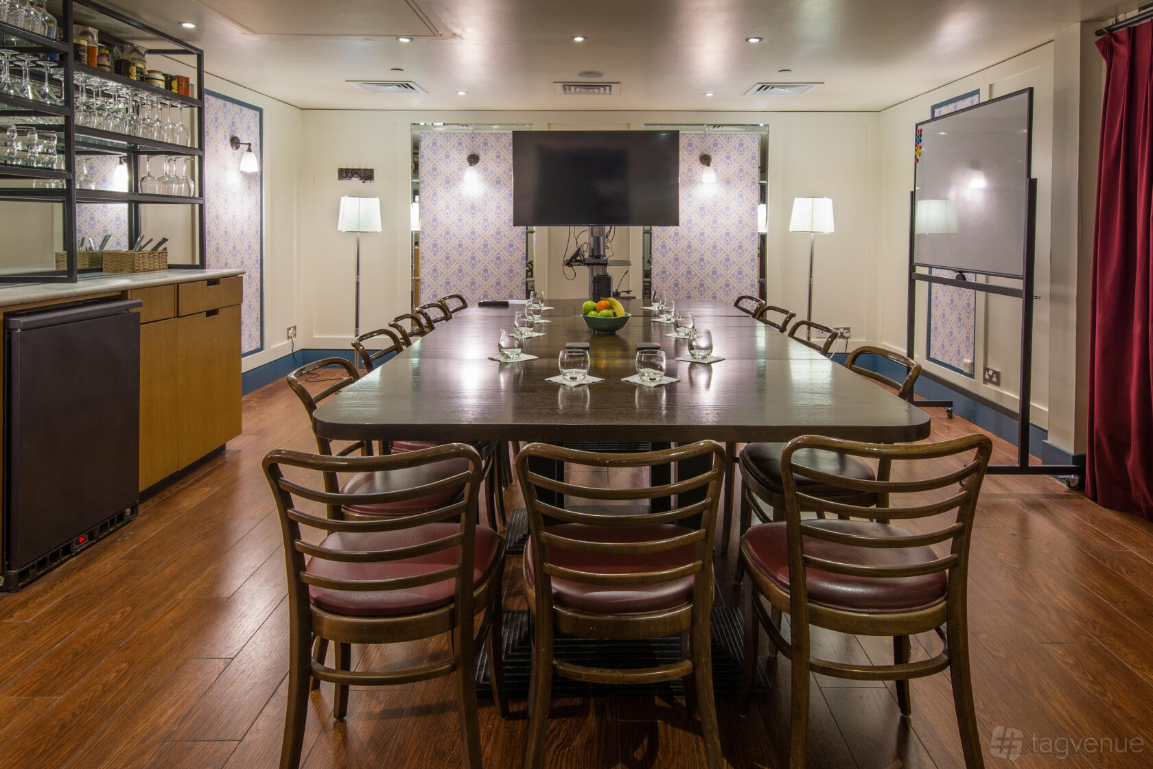 A restaurant meeting room with a long wooden table, chairs, wall-mounted TV, and glassware at Cote Brasserie St. Paul's.