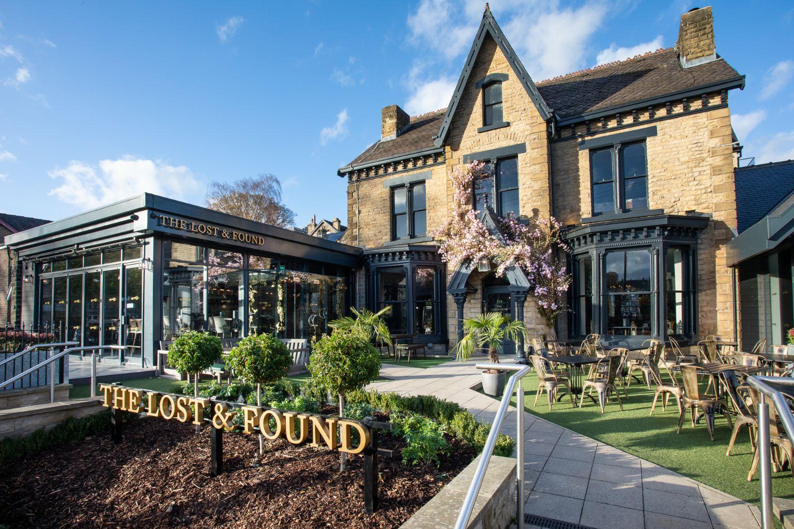 A restaurant with a historic stone exterior, glass-enclosed dining area, and outdoor seating at The Lost and Found Sheffield.