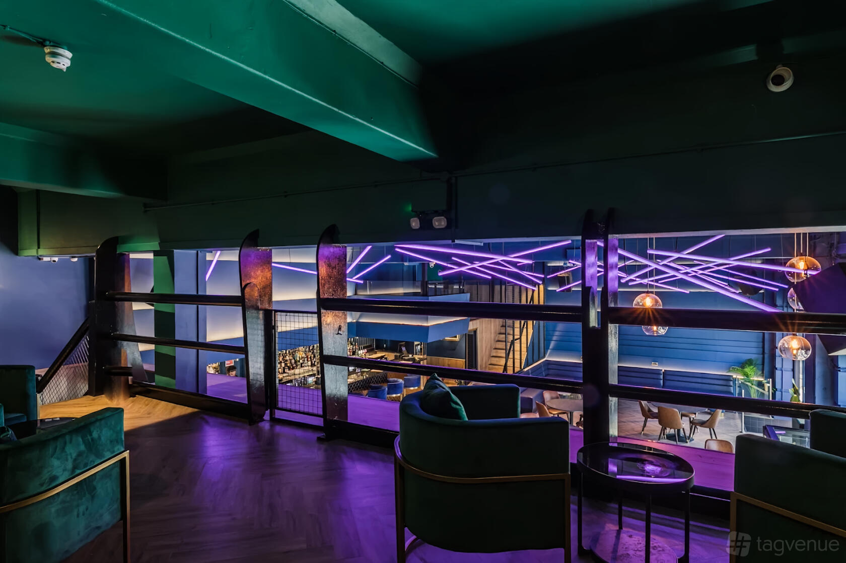 An event space with neon purple ceiling lights, dark green velvet seating, and a balcony view at THE CAMDEN.