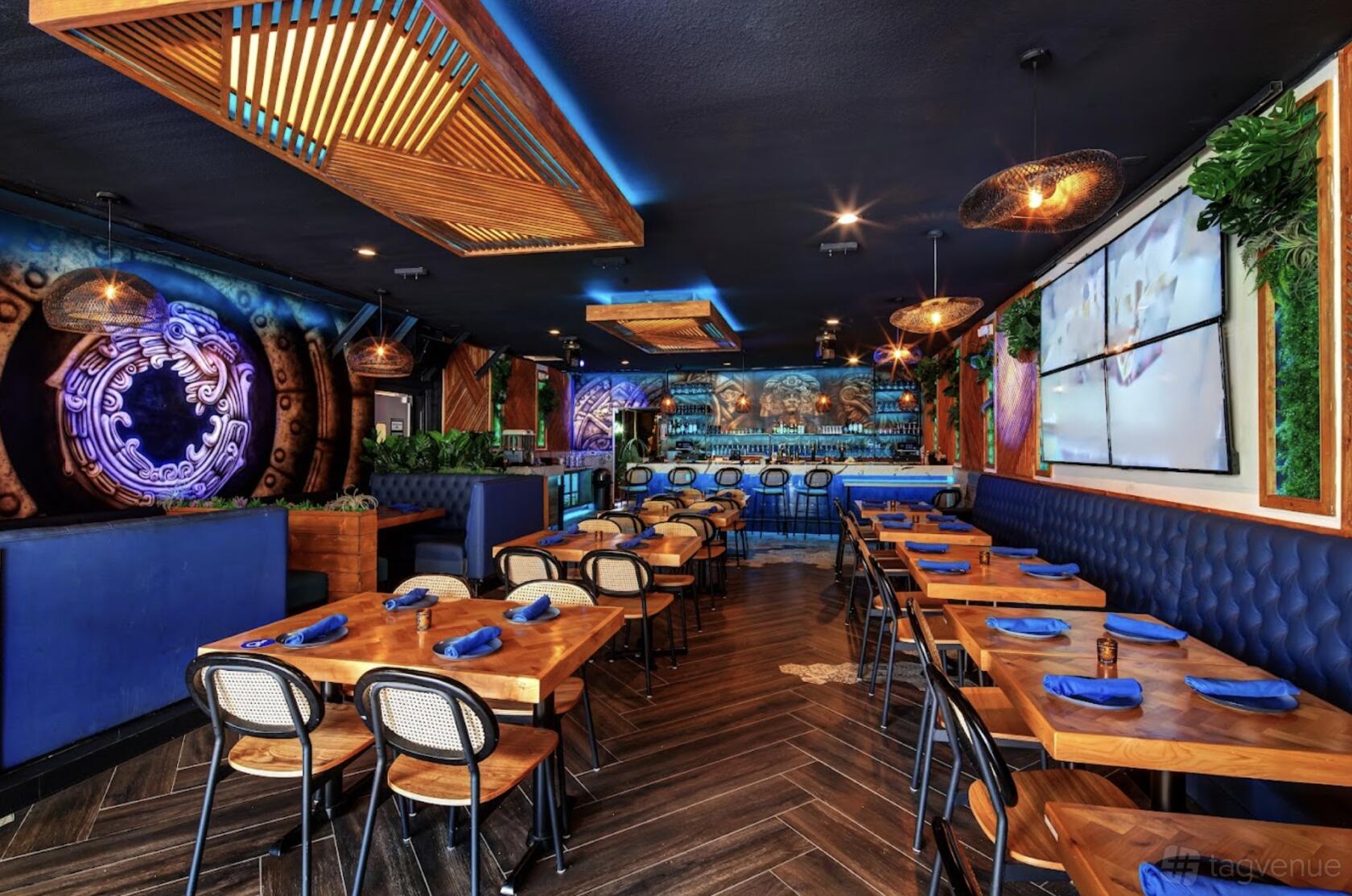 A restaurant with wooden tables, blue napkins, wall murals, and geometric ceiling lights at Estrella Taqueria Lounge.