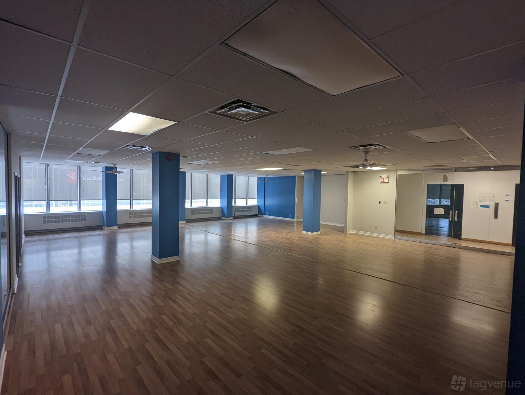 An open event area with large windows, wood flooring, and blue accent walls at The Village Hive Eglinton.