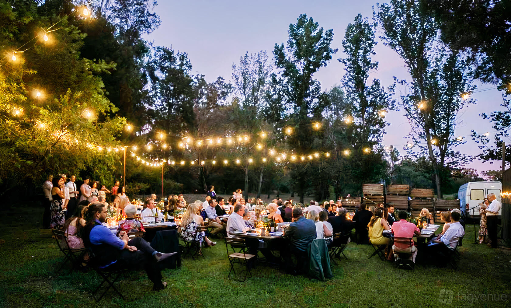 An outdoor venue with string lights, long tables, and guests dining on a grassy lawn at John Gehrig Wines Oxley.