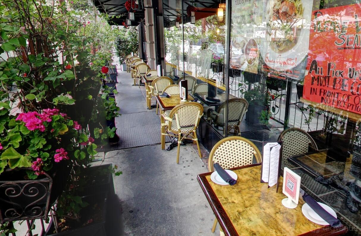 An outdoor dining area with bistro tables, woven chairs, and lush potted plants at Amante Restaurant.