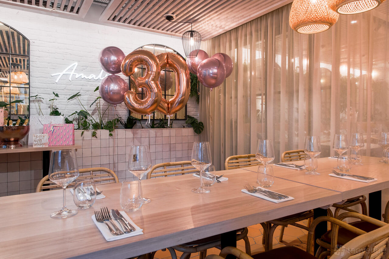 A restaurant dining area with pink balloon decorations, set tables, and cane chairs at Amalfi Ristorante.