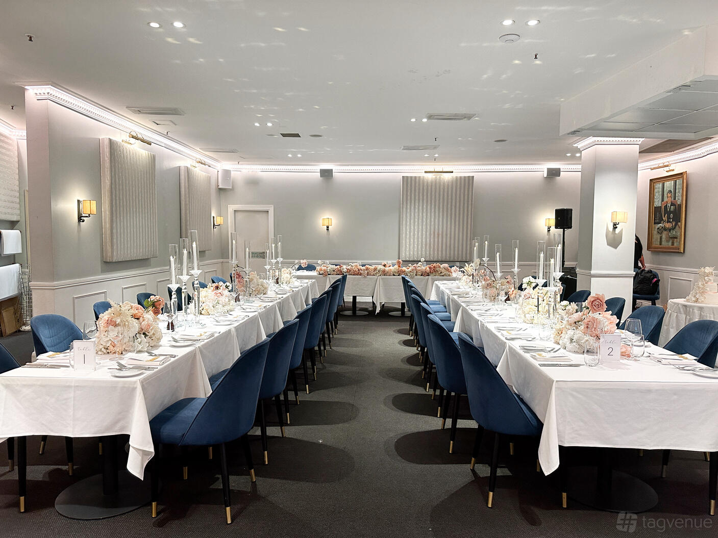 A dining room with white-clothed tables, blue velvet chairs, floral centerpieces, and candelabras at The Royal Exchange of Sydney.