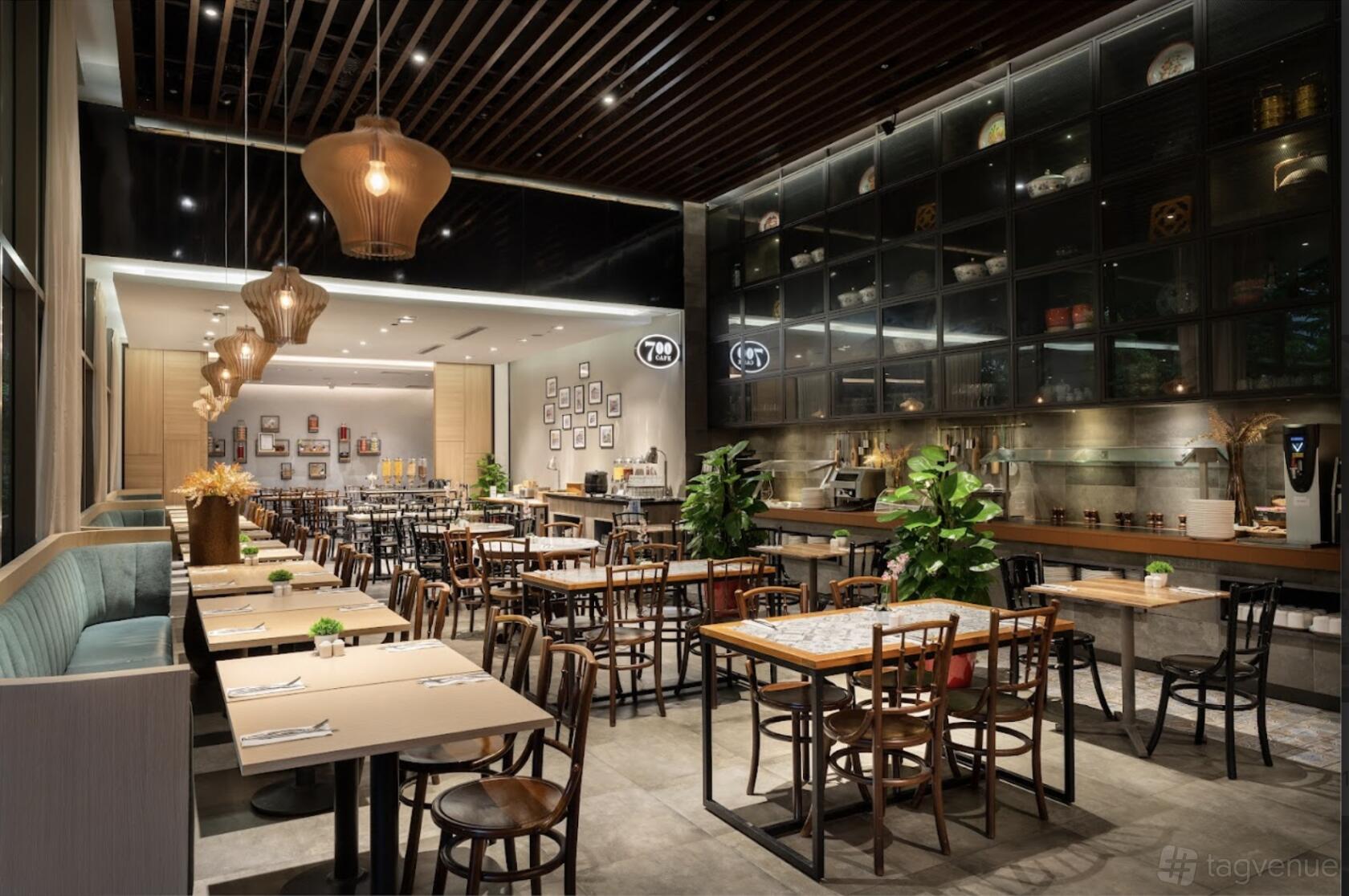 A hotel cafe with wooden tables, pendant lighting, banquette seating, and decorative wall shelves at Hotel Traveltine.