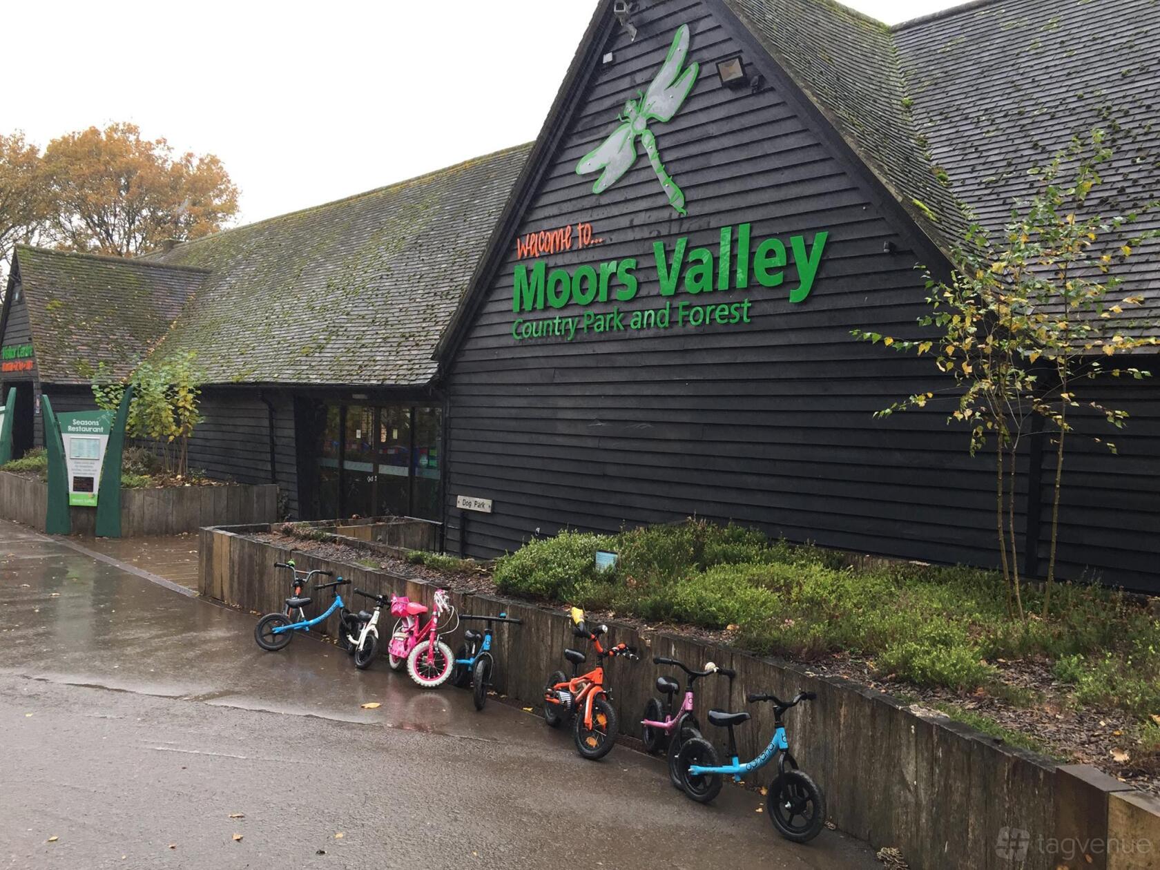 An outdoor venue with a black timber building, green signage, and children's bikes parked outside at Go Ape Moors Valley.