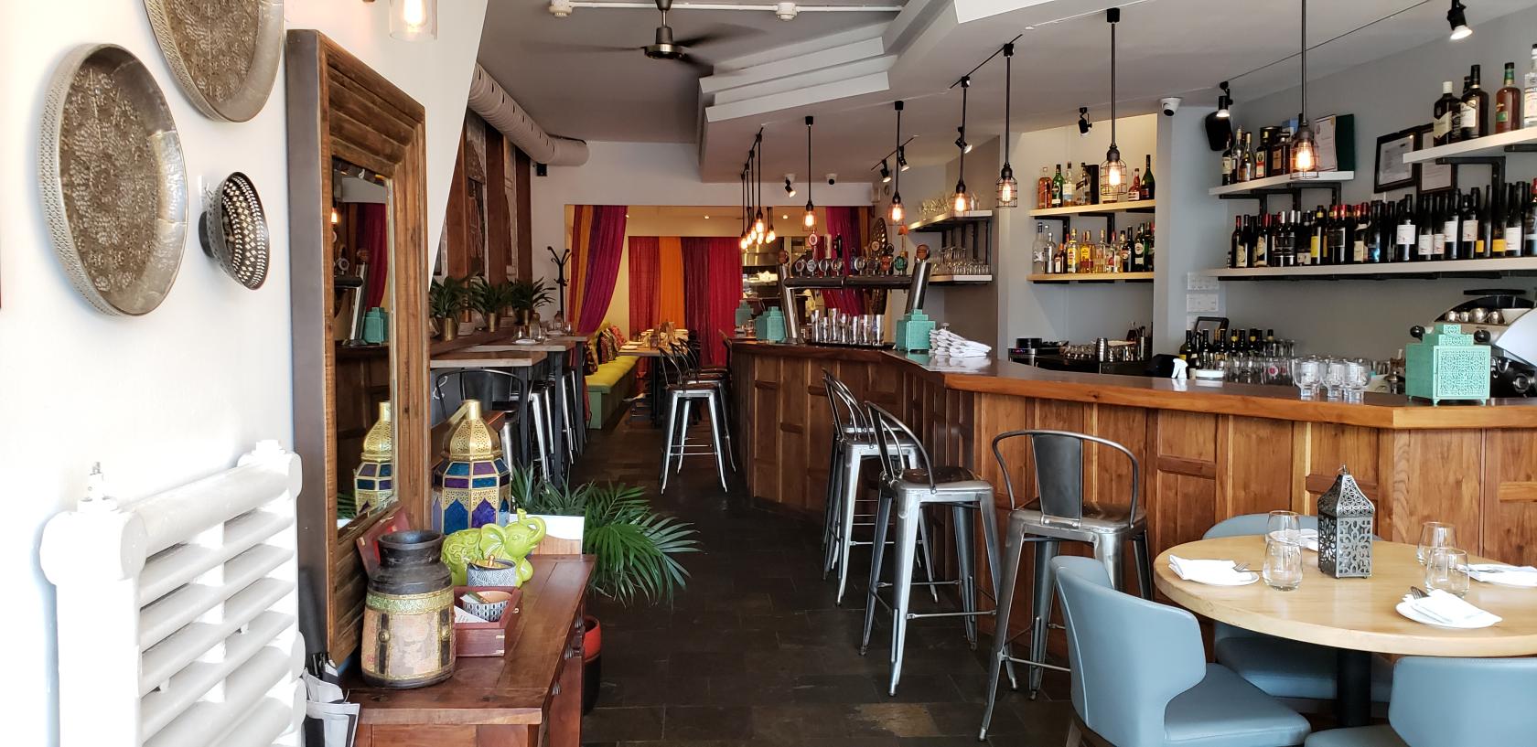 An event space in a restaurant with a wooden bar, high metal stools, pendant lighting, and decorative lanterns at Cumin Kitchen.