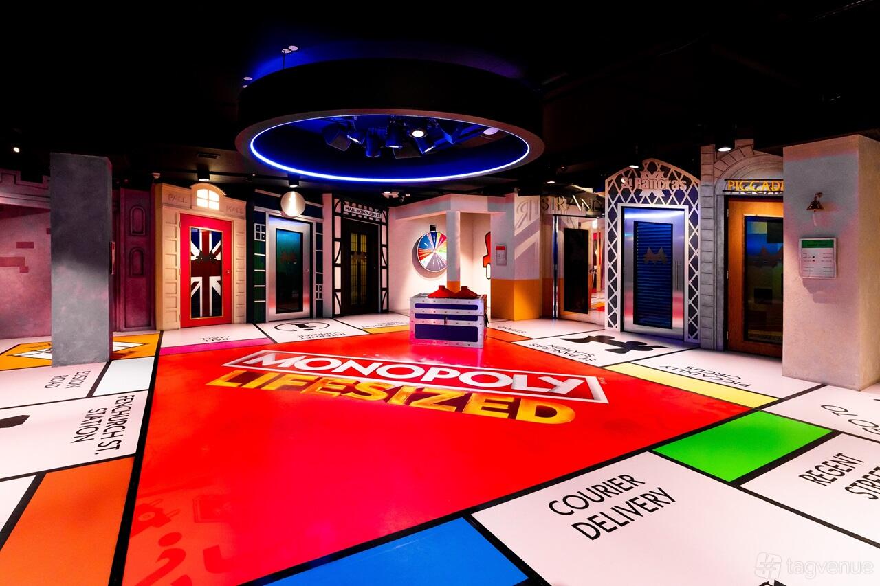 An event venue with a giant MONOPOLY LIFESIZED game board, colorful themed doors, and overhead lighting at MONOPOLY LIFESIZED.