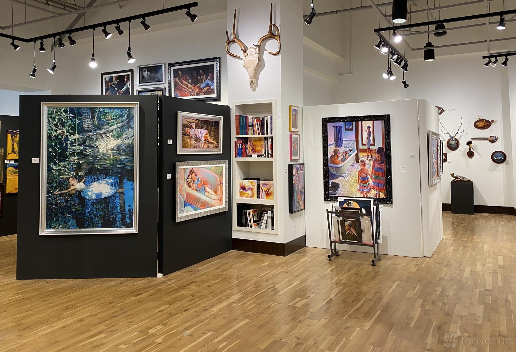 A gallery with hardwood floors, black partition walls displaying colorful art, and track lighting at Ao5 Gallery.