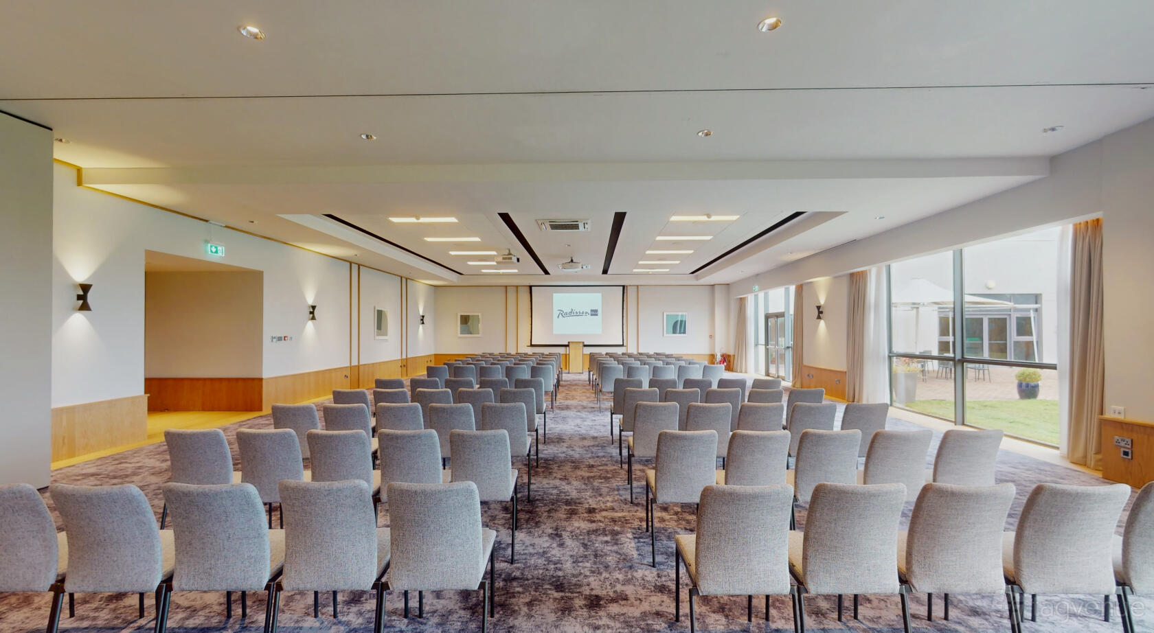 An auditorium with rows of grey chairs, carpeted flooring, and large windows at Radisson Blu Hotel, Dublin Airport.