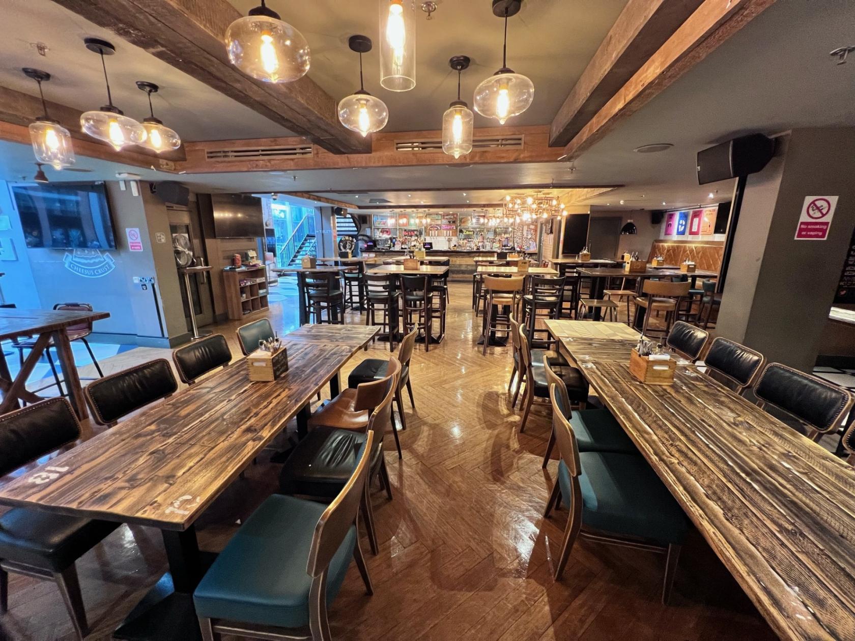 An event space with long wooden tables, mixed chairs, and pendant lighting at Tank and Paddle Bishopsgate.