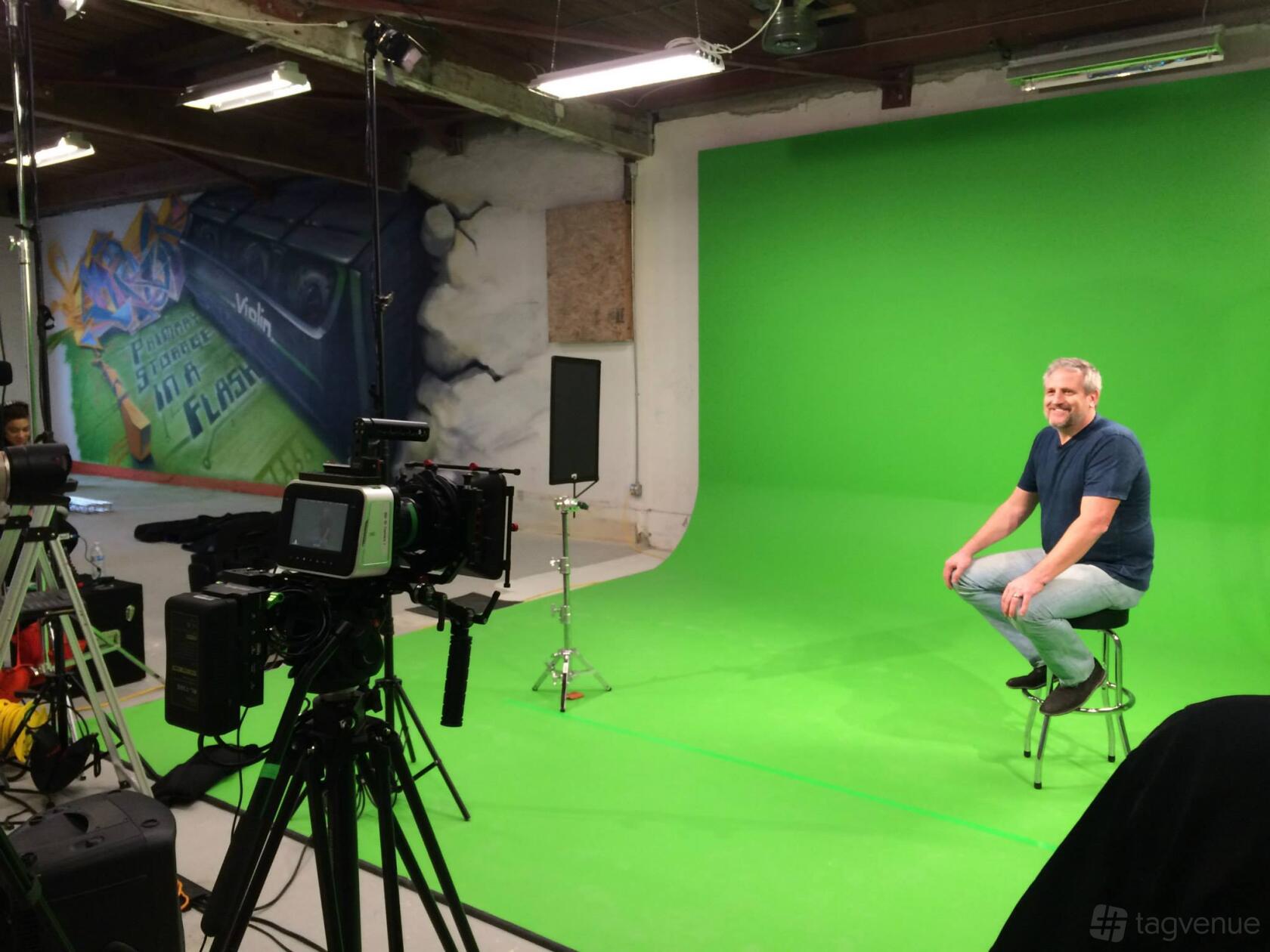 A photo studio with a large green screen backdrop, professional cameras, and overhead lighting at Trilogy Visual Media.