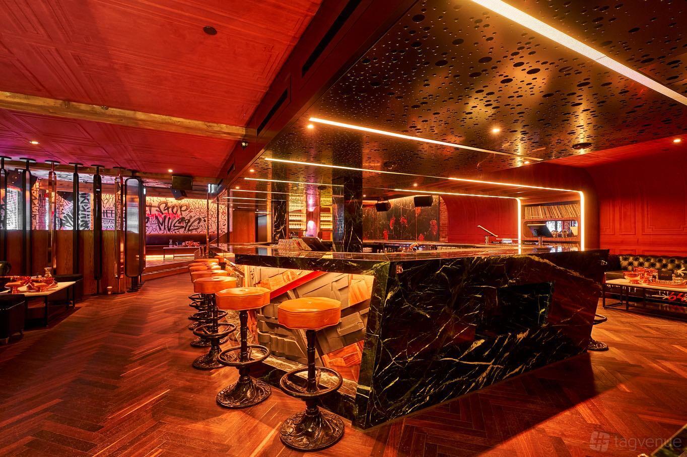 A bar with a black marble counter, amber leather stools, wood floors, and red ceiling at Deer Lady.