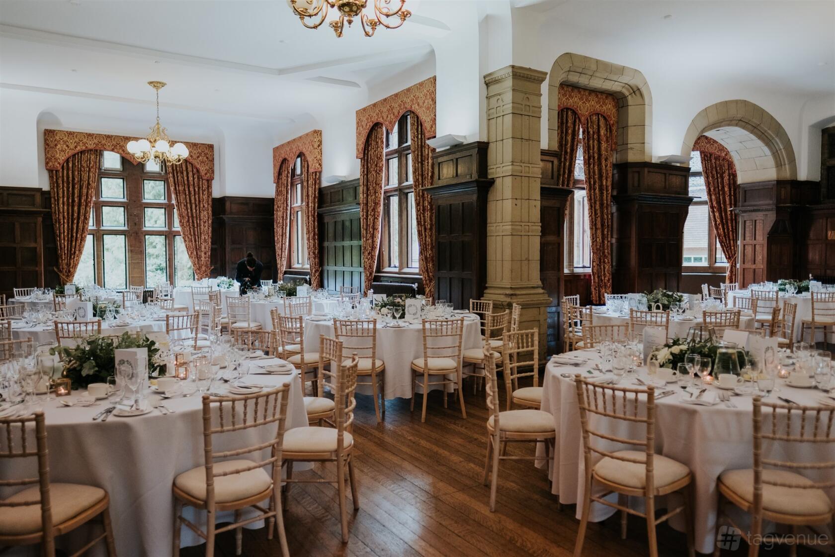 An event venue with tall arched windows, wood paneling, and round tables with white linens at Marden Park Mansion.