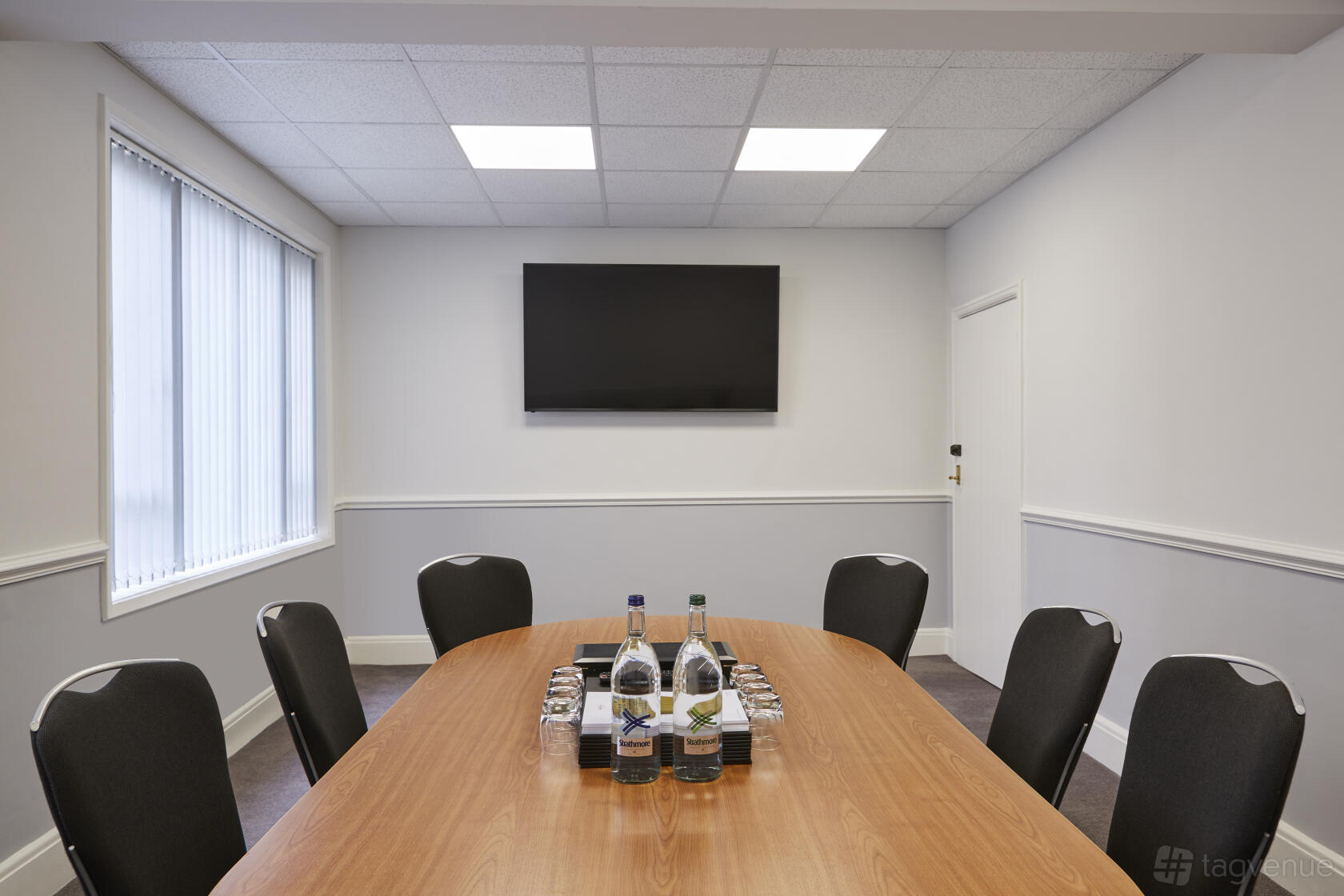 A boardroom with a wooden oval table, black chairs, bottled water, and a wall-mounted screen at Mercure Sheffield Kenwood Hall Hotel & Spa.