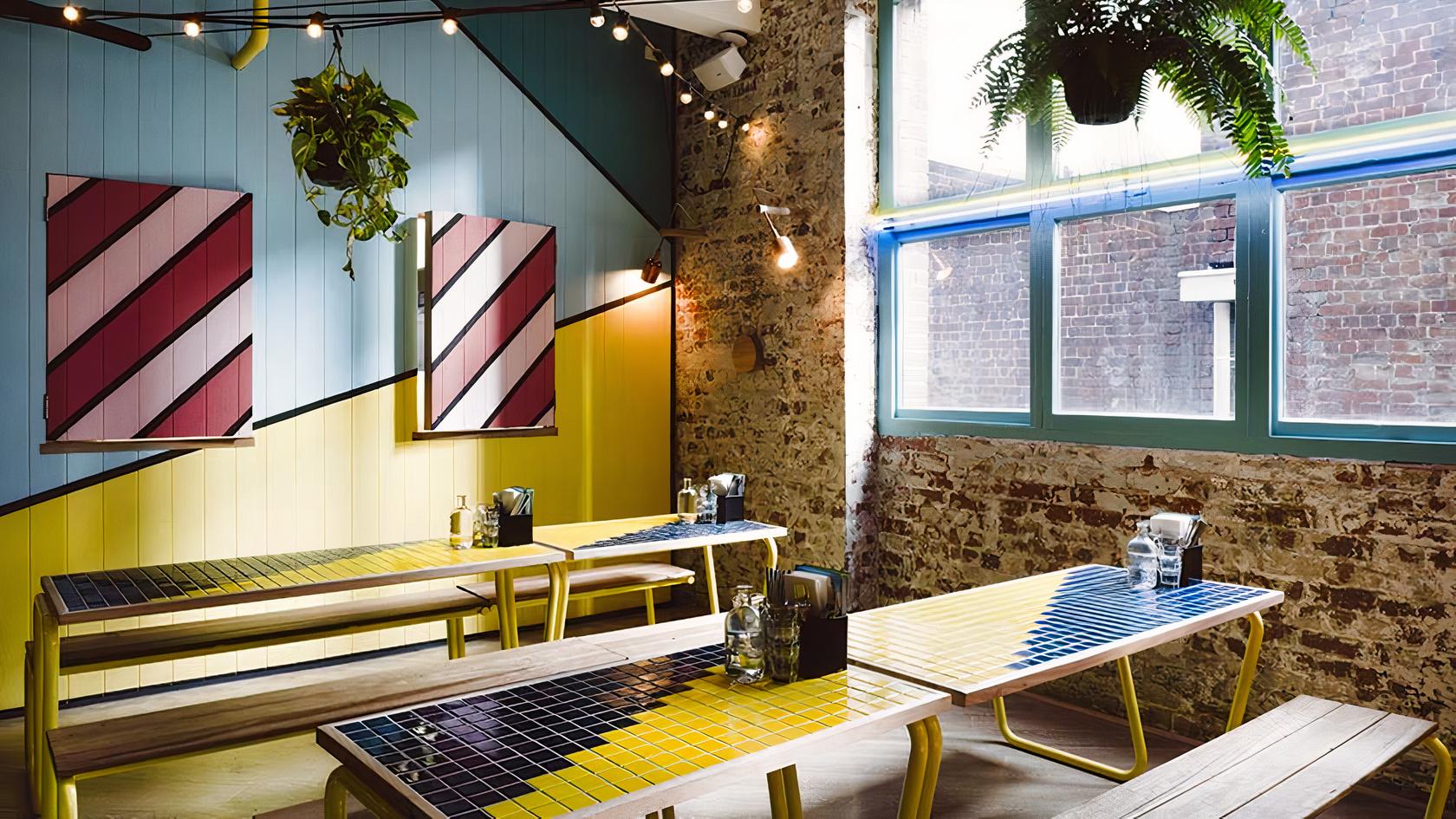 A dining room with colorful tiled tables, exposed brick walls, string lights, and large windows at Fonda Mexican @ Flinders Lane.
