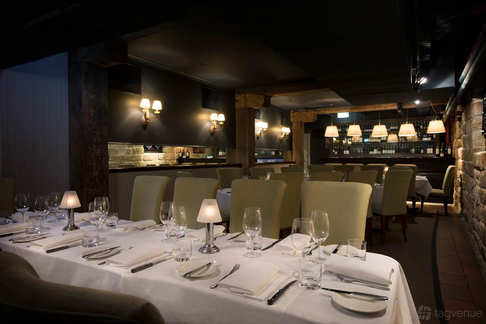 An intimate restaurant with soft wall lighting, stone accents, and tables set with white linens at Kingsleys Australian Steakhouse.