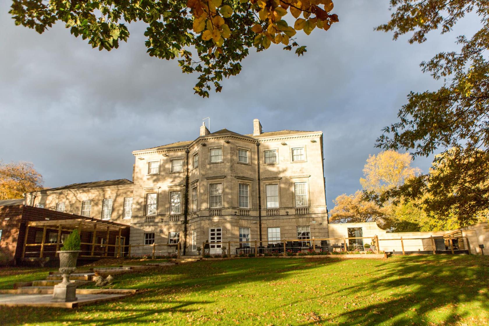 A historic hall with large windows, stone exterior, and spacious lawn surrounded by trees at Aston Hall.