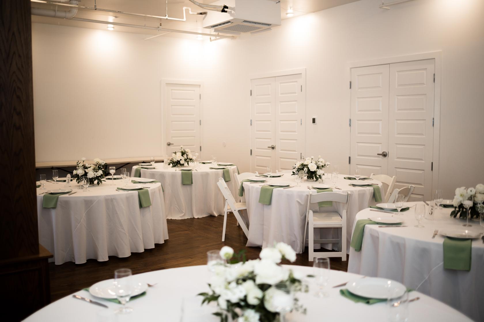 An event space with round tables, white linens, green napkins, and floral centerpieces at 11th Avenue Events.