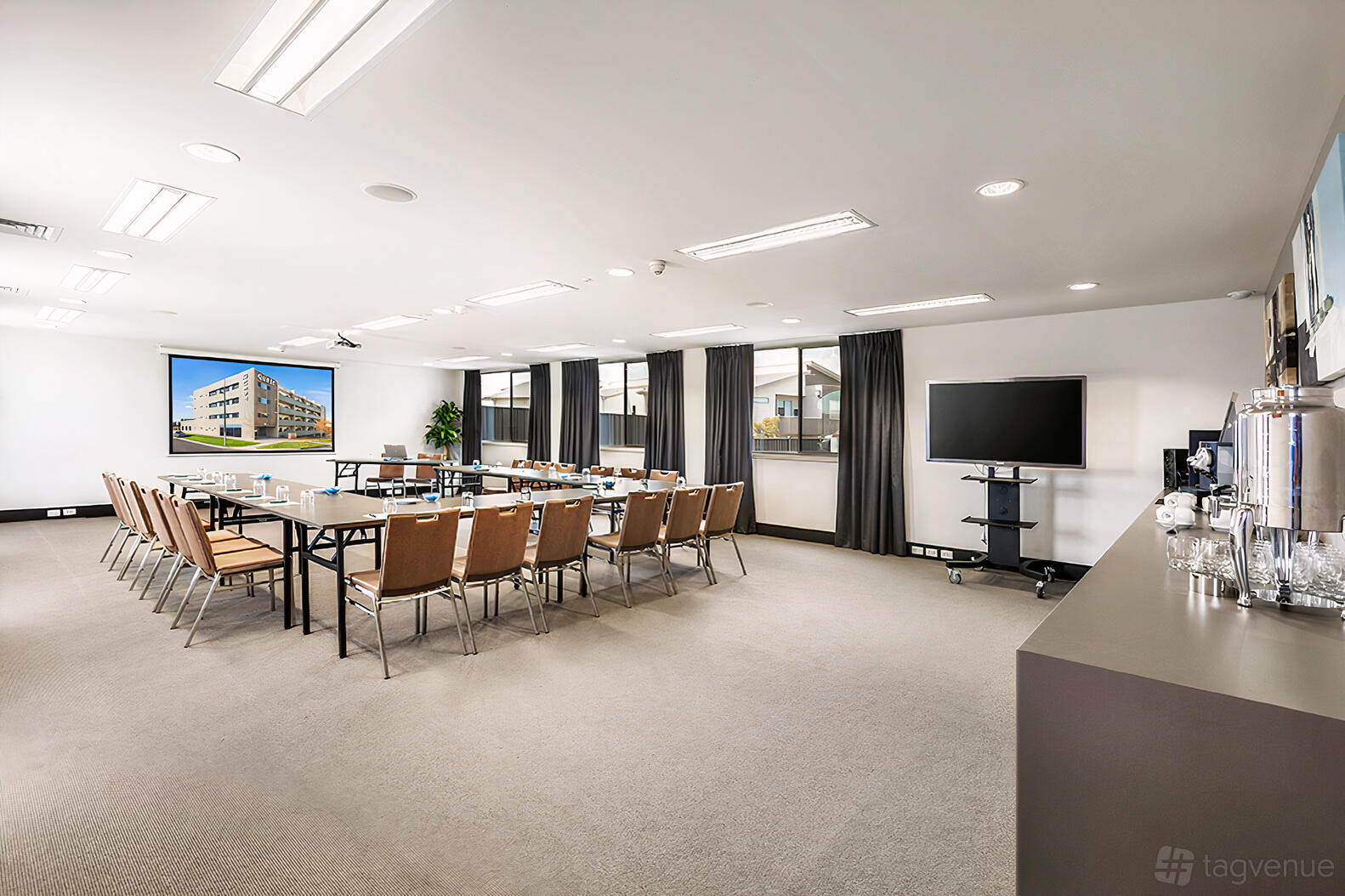 A conference room with U-shaped tables, brown chairs, large windows, and a refreshment station at Quest Bundoora.