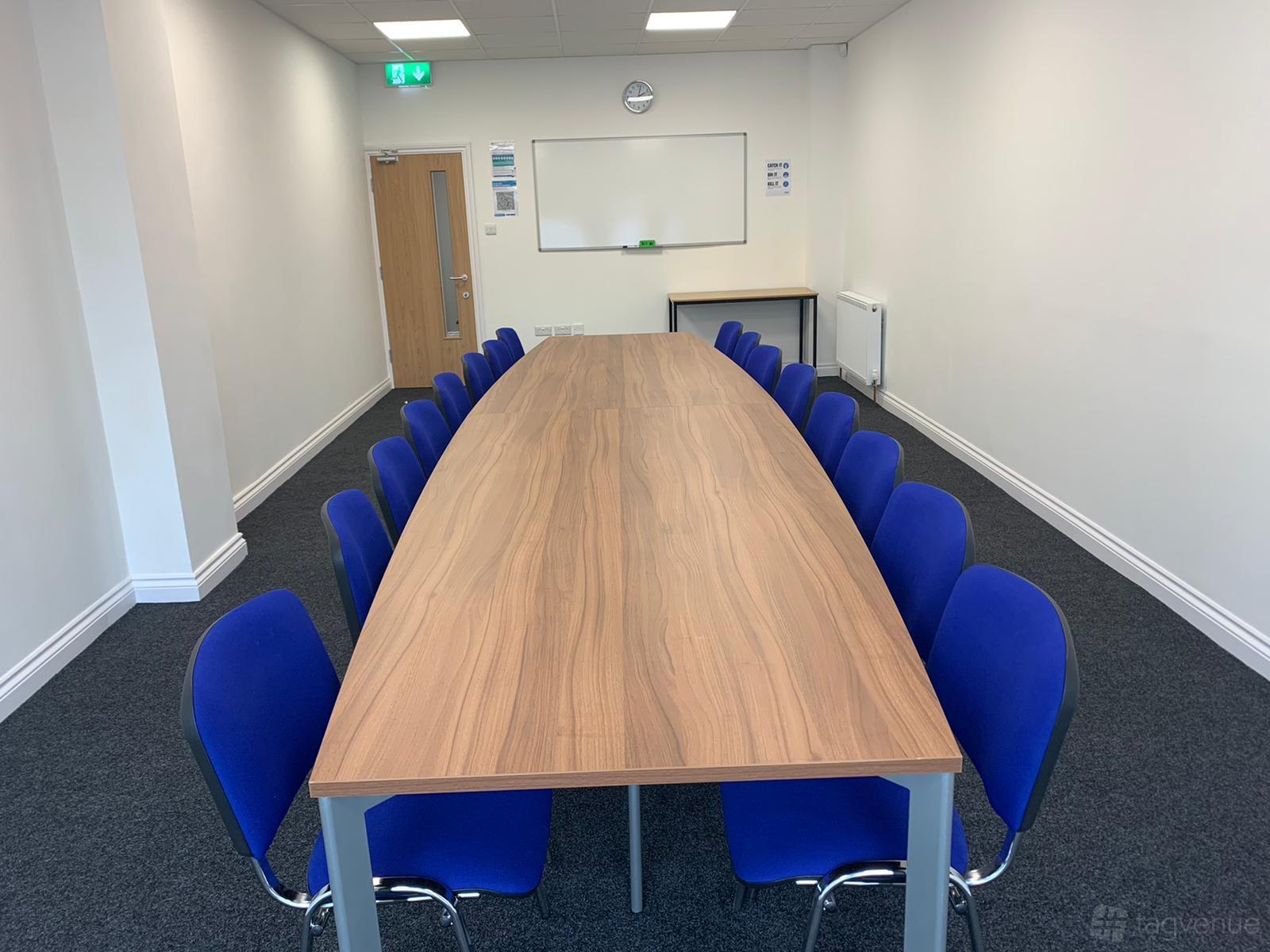 A meeting room with a long wooden table, blue chairs, a whiteboard, and a clock at Bridge Corporation Properties Ltd.