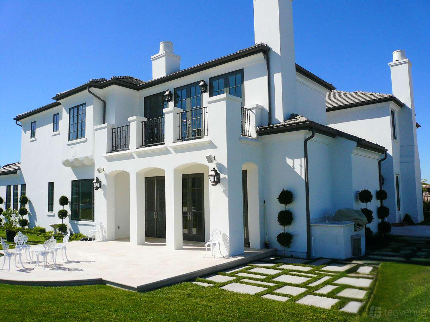 A country house with white stucco exterior, black-framed windows, and a patio with outdoor seating at LUXURIOUS FRENCH COUNTRY ESTATE.