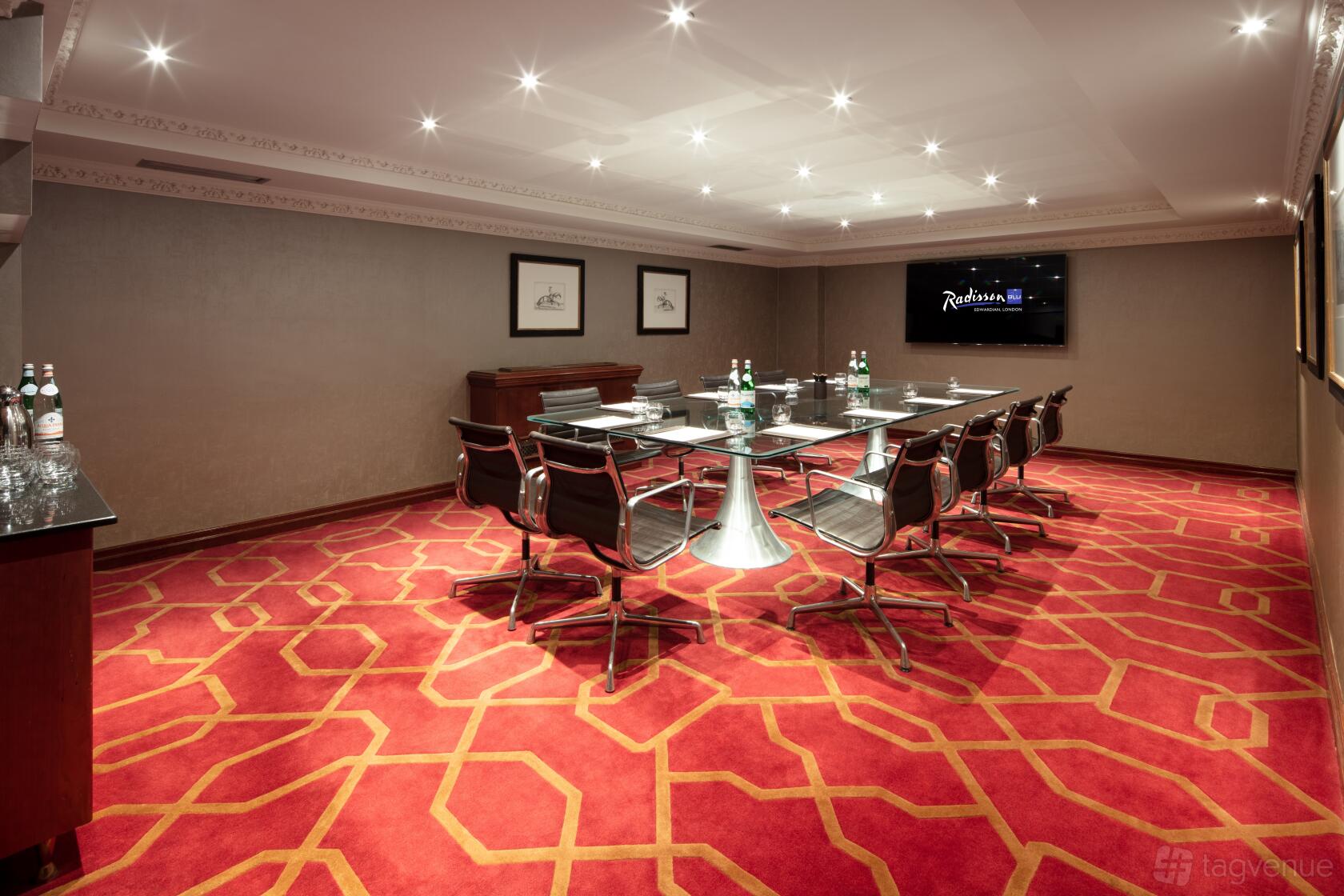 A meeting room with a red patterned carpet, boardroom-style table, and wall-mounted screen at Radisson Blu Hotel, London Heathrow.