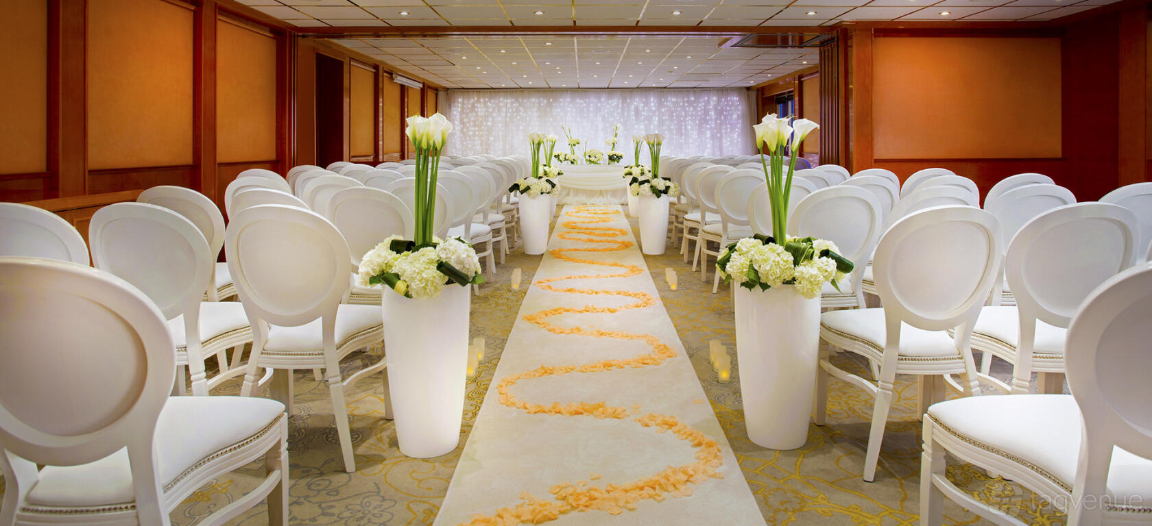 An event space with white chairs, tall floral arrangements, and a petal-lined aisle at Sunborn London Yacht Hotel.