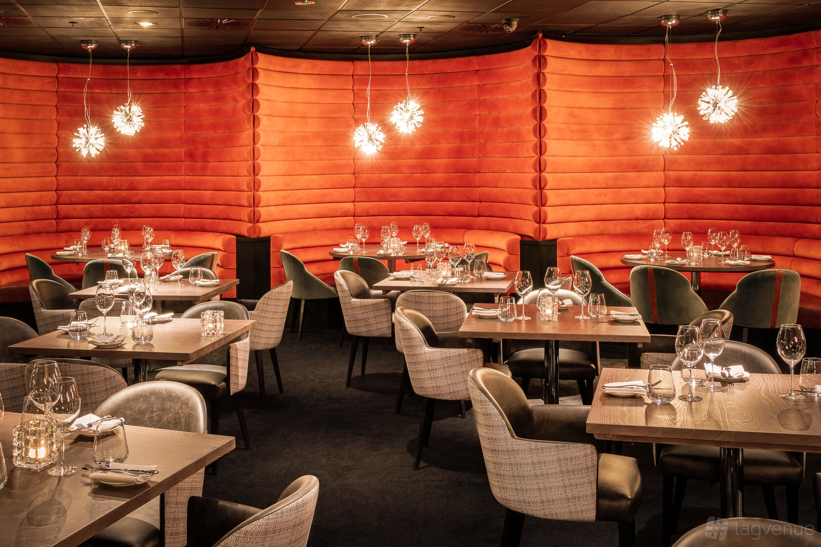 A dining room with orange padded walls, round pendant lights, and set tables with glassware at Gaucho O2 Arena.