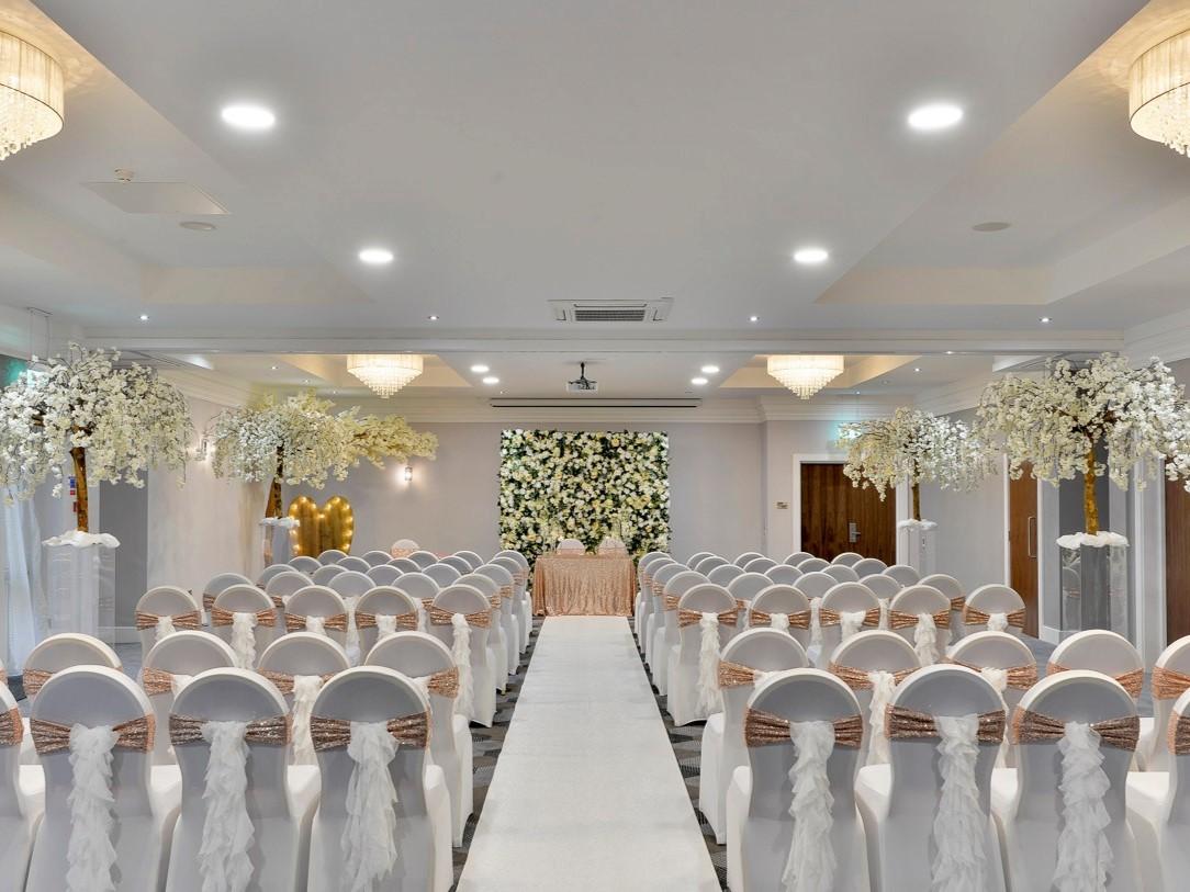 An event space with rows of white chairs, floral aisle decor, and a flower wall backdrop at Mercure Norton Grange Hotel and Spa.