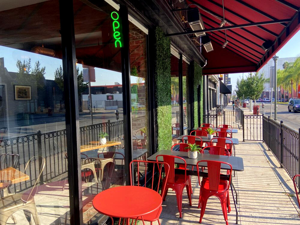 An outdoor restaurant patio with red metal chairs, potted plants, and large windows at Sumac Mediterranean Cuisine.