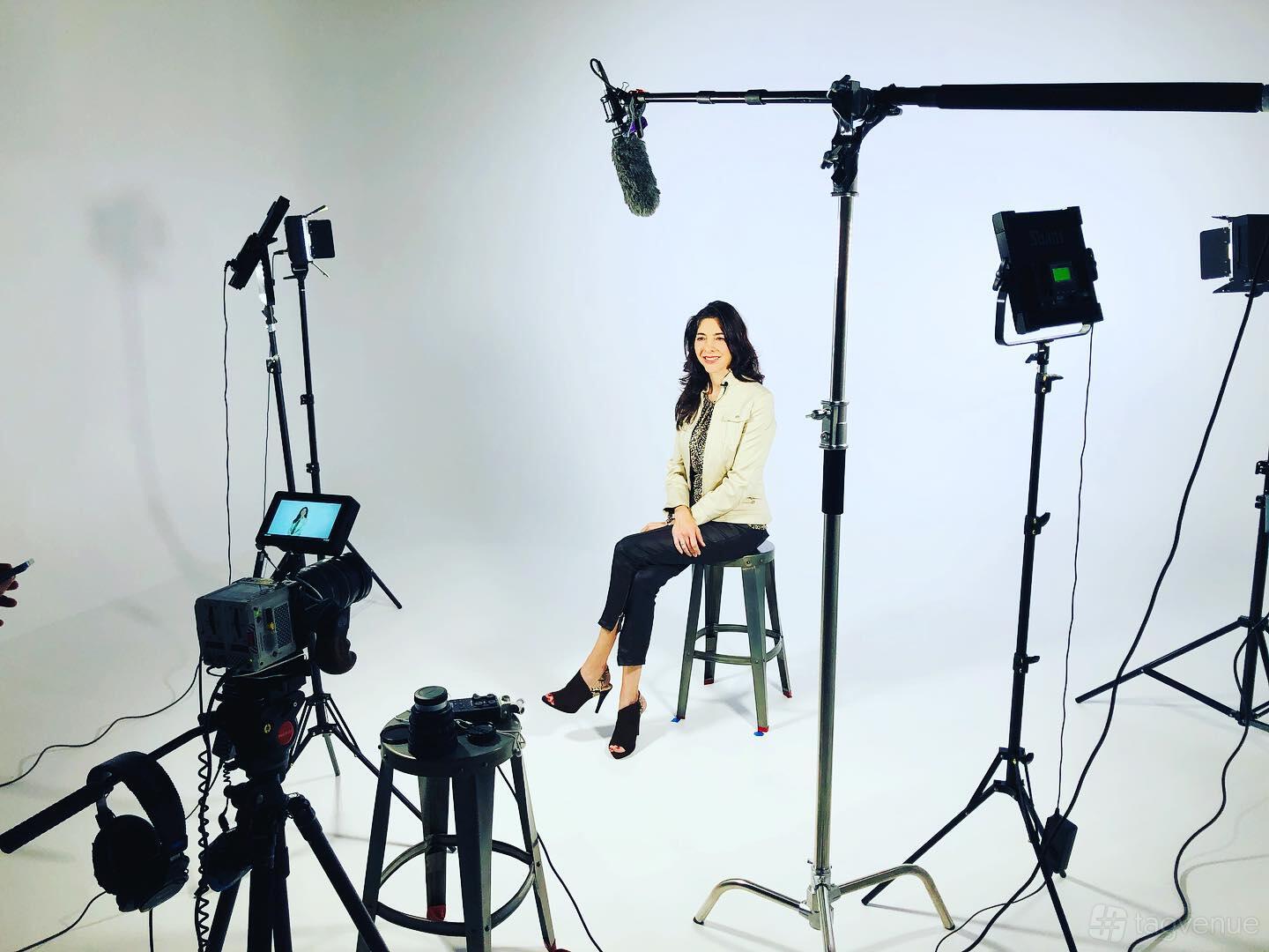 A film studio with a seamless white cyclorama wall, video cameras, lighting rigs, and a stool at Alamo City Studios.