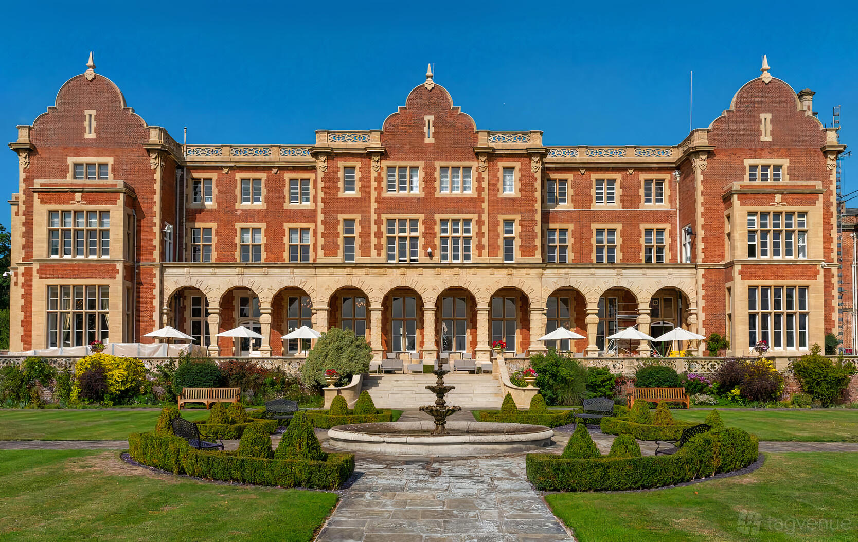 A historic building with a red brick facade, arched windows, and landscaped gardens with a central fountain at Easthampstead Park.