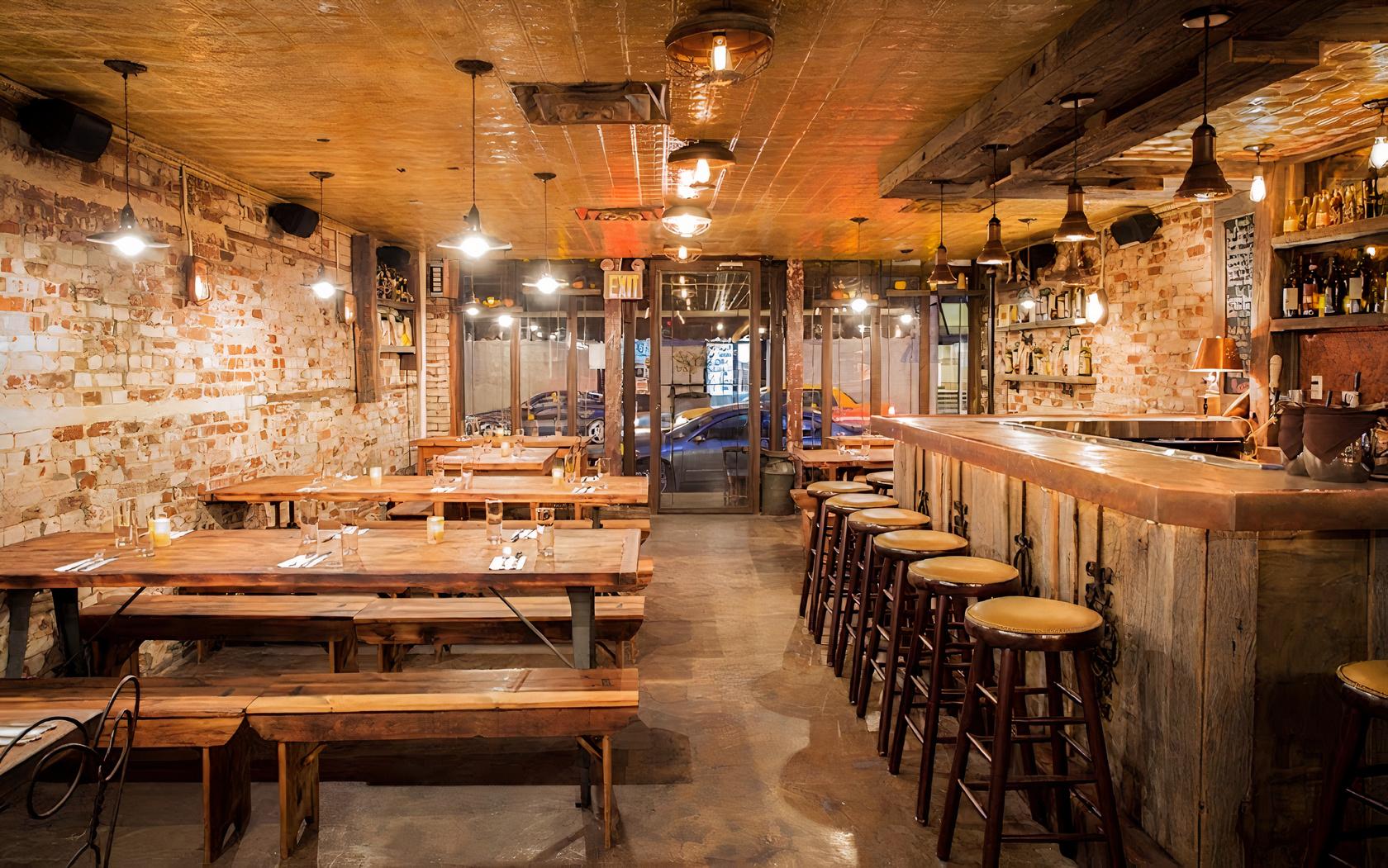 A restaurant with exposed brick walls, wooden communal tables, and a bar with backless stools at Piacere.
