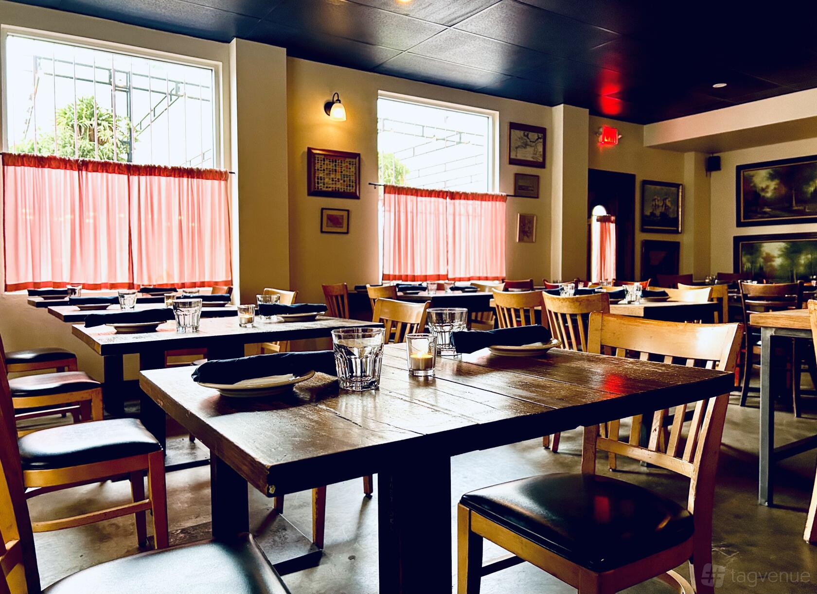 A restaurant with wooden tables, matching chairs, red curtained windows, and wall art at Mimo.