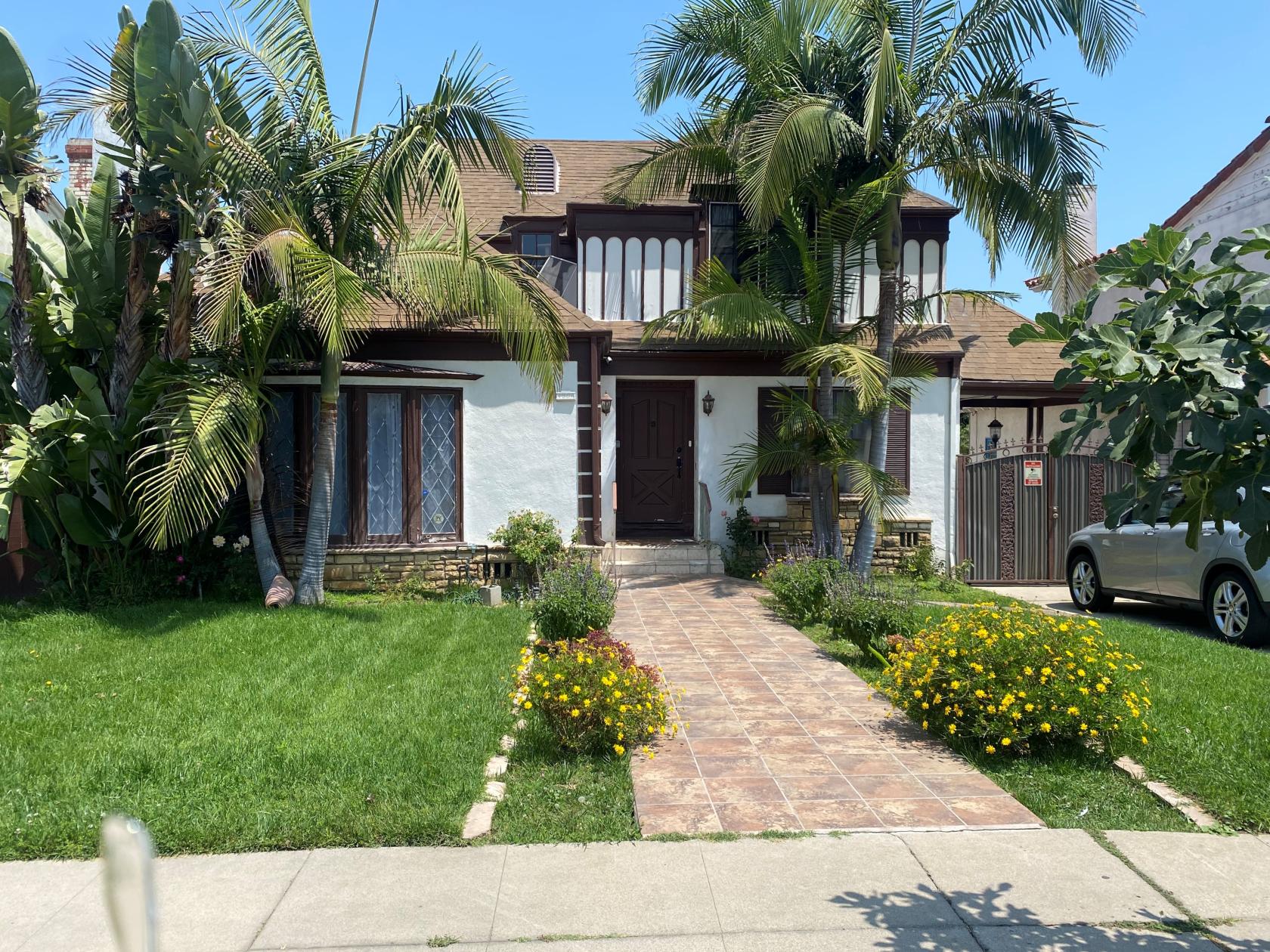 An open air venue with lush green lawn, palm trees, and a tiled walkway leading to the house at LA Manor.