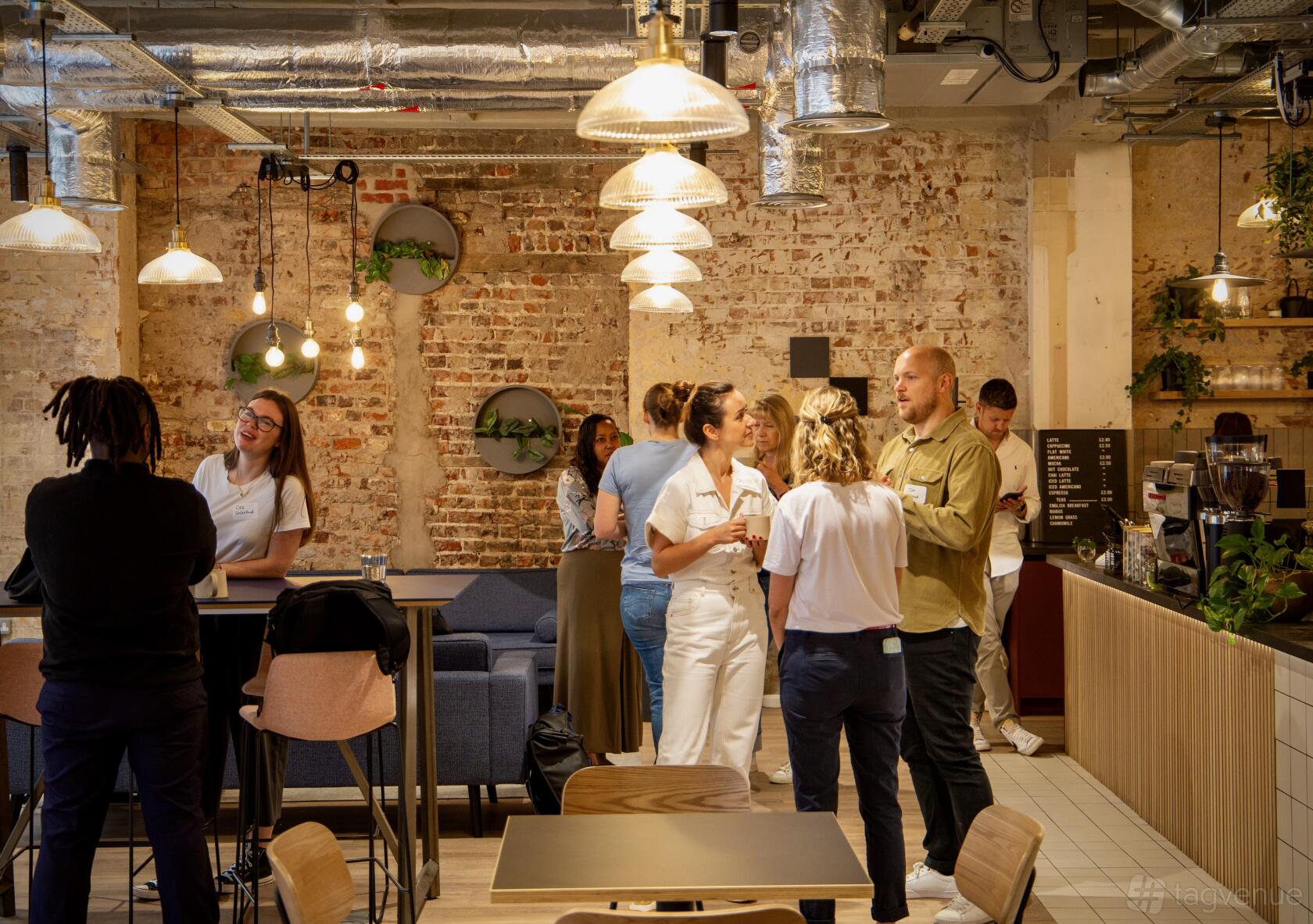 A coworking cafe with exposed brick walls, pendant lighting, and a coffee counter at Techspace Worship Street.