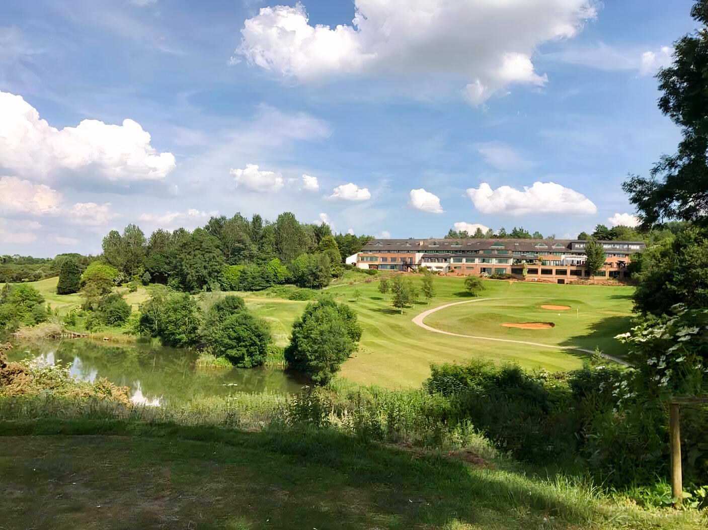 A hotel with landscaped golf course, sand bunkers, and a pond surrounded by trees at Hellidon Lakes Hotel.