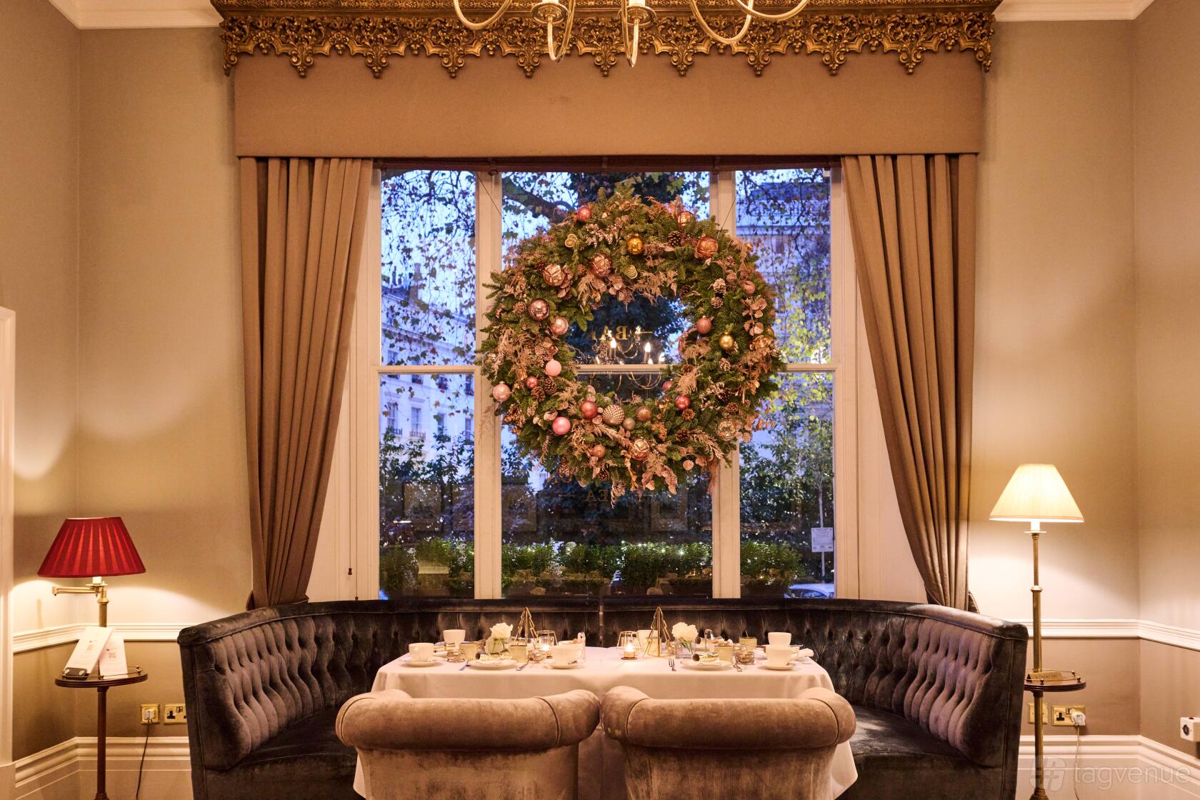 A restaurant dining area with a large floral wreath, velvet banquette seating, and elegant table settings at The Hyde Restaurant & Bar.